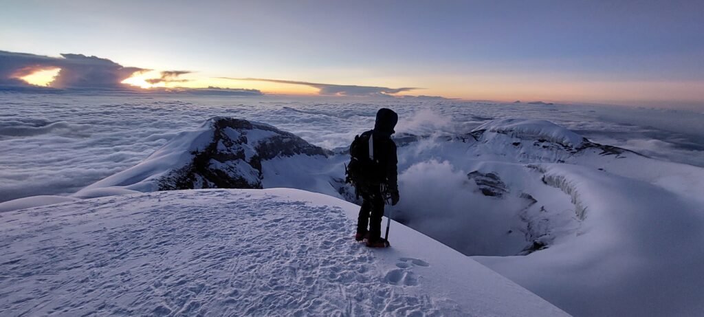 Climber standing at the summit of Cotopaxi at sunrise overlooking the crater
